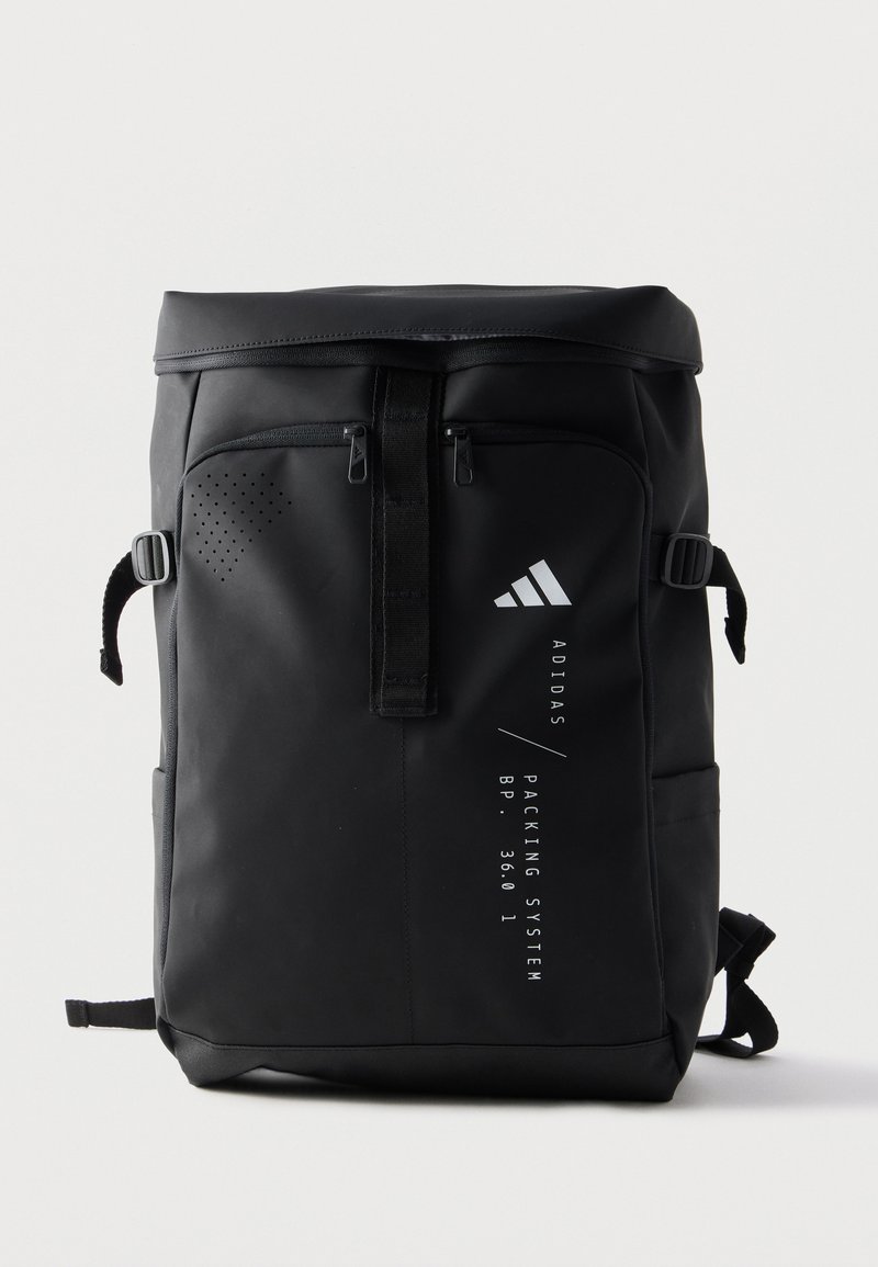 Sac à dos rectangulaire noir Adidas avec fermeture roll-top, poches zippées frontales, boucles latérales et logo blanc vertical avec texte sur le panneau avant.