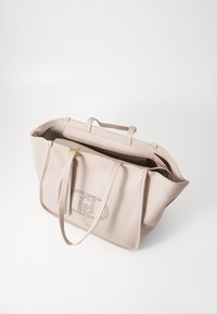 Borsa tote beige con texture, due manici, chiusura con zip e dettagli perforati sulla parte frontale. Interno spazioso con una tasca aggiuntiva.