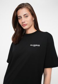 T-shirt in cotone nero con collo a giro, vestibilità ampia e logo stampato in bianco sul lato sinistro del petto che recita "ALLSAINTS LONDON."