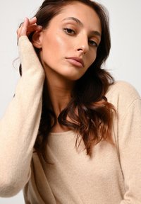 Beżowy sweter z okrągłym dekoltem i długimi rękawami. Miękka tekstura, dopasowany krój, z delikatnymi detalami przy krawędziach.