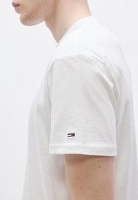 Λευκό βαμβακερό t-shirt με κοντά μανίκια, με μικρό κεντημένο λογότυπο σε κόκκινο, λευκό και μπλε στο αριστερό μανίκι.