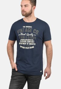 Marineblå bomulls T-skjorte med korte ermer og rund hals; har vintage-inspirerte grafikker i kremfarge. Glatt tekstur, avslappet passform.
