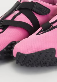 Baskets roses Puma avec des sangles noires réglables et des semelles noires texturées cloutées, conçues pour l’adhérence et le confort.