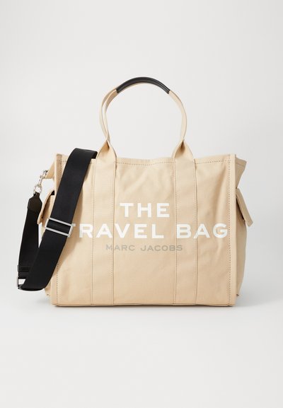 Borsa da viaggio in canvas beige con manici neri e tracolla staccabile. Presenta un grande testo bianco, "LA BORSA DA VIAGGIO", sul davanti.
