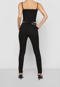 Jeans negros ajustados con una cintura alta, bolsillos traseros y una textura de denim suave, combinados con una camiseta ajustada negra.