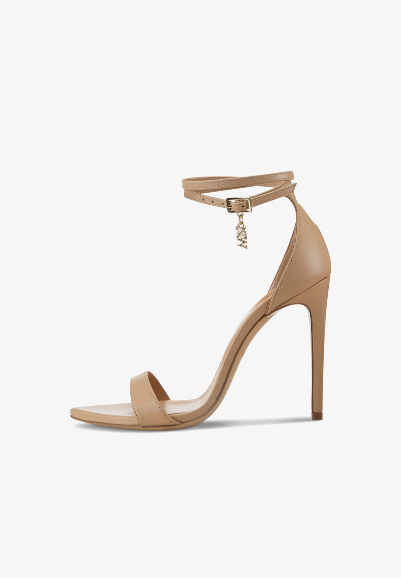 Nude hoge hak sandaal met een dunne enkelband, vierkant teengedeelte en een gouden hanger aan de gesp. Gladde leren textuur en elegante silhouet.