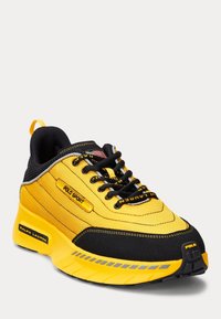 Gul och svart atletisk sko med nät- och mockamaterial, vadderad krage, snörning och logotypdetaljer på sidan och hälen.