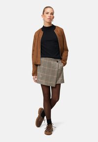 Braune Wildleder-Bomberjacke, schwarzes figurbetontes Oberteil, Karo-Wickelrock mit Knopf, schwarze Strumpfhose und braune Schnürschuhe mit dicken Sohlen.