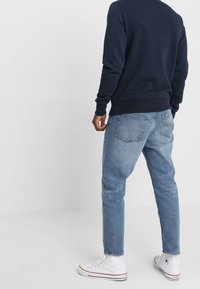 Sudadera de cuello redondo en navy, vaqueros ceñidos de color azul claro y zapatillas blancas con acentos rojos. Tejido suave, ajuste casual y diseño minimalista.