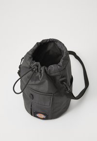 Zwarte stoffen trekkoordtas met een cilindrische vorm, verstelbare schouderband, buitenzak en logo-opdruk. Gladde textuur met minimale stiksels.