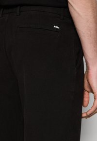 Černé kalhoty vyrobené z texturované tkaniny s úzkým střihem, s zadní kapsou a bílou nášivkou BOSS poblíž pasu.