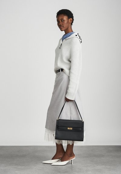 Suéter branco de malha, saia cinza com bainha de renda, bolsa preta com ferragens douradas e sapatos de salto branco com ponta. Modelo de pé em perfil.