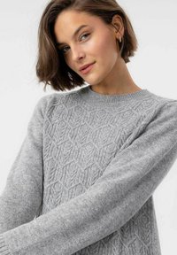Hellgrauer Pullover mit einem strukturierten Wabenmuster, geripptem Ausschnitt und langen Ärmeln. Der Stoff scheint weich und gestrickt zu sein.