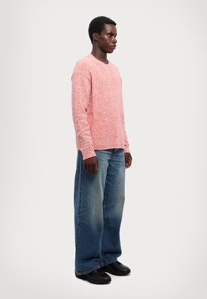 Rot-weißer, gesprenkelter Langarmpulli mit Rundhalsausschnitt, kombiniert mit lockeren blauen Jeans und schwarzen Schuhen.