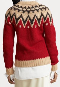 Pull en maille avec un corps rouge, un ourlet côtelé beige et un empiècement à motifs en beige, noir et blanc. Il présente des manches longues et une coupe décontractée.