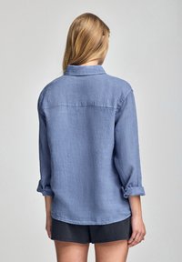 Ljusblå, långärmad skjorta med knappar och uppvikta manschetter samt en detalj på ryggen. Tillverkad av textil med en avslappnad passform.