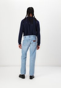 Blugi de denim bleu deschis cu croială dreaptă și o etichetă din piele pe buzunarul din spate. Asortați cu o cămașă albastră închis cu mânecă lungă și pantofi negri.