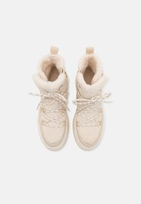 Beige kotníkové boty s nadýchanou ovčí kožešinou, kulatou špičkou, polstrovaným límcem a kovovými oky na šňůrky. Mají plochou gumovou podrážku.