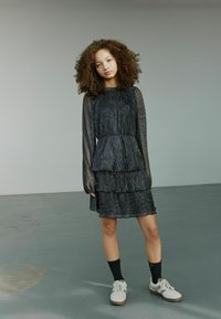 Čierne šaty s viacerými vrstvami a dlhými priesvitnými rukávmi s textúrovaným vzorom. Nosené s bielymi teniskami a čiernymi ponožkami.