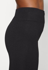 Nära bild av en person som bär högmidjade, räfflade svarta leggings, som visar sidoprofilen från midjan till övre låret.