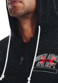 Czarna bluza z kapturem w kropeczki, z białymi sznurkami, zamkiem z przodu oraz haftowanym logo "Under Armour ATH. DEPT." w czerwonych i białych akcentach.
