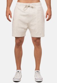 Pantaloni corti di cotone color beige chiaro con elastico in vita e cordoncino. Lunghezza corta, tasche laterali e dettaglio logo ricamato sull'orlo.