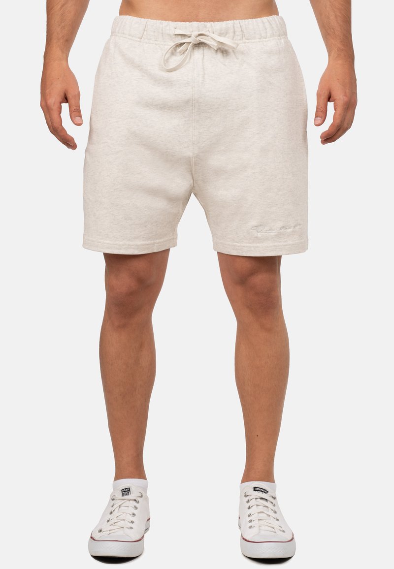 Pantaloni corti di cotone color beige chiaro con elastico in vita e cordoncino. Lunghezza corta, tasche laterali e dettaglio logo ricamato sull'orlo.