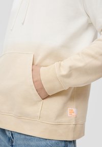 Sudadera de color claro con diseño ombré, que incluye un bolsillo, puños acanalados y una etiqueta visible en el dobladillo. Textura de tela suave.