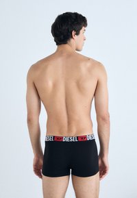 Caleçons boxers noirs avec une ceinture rouge et blanche Diesel, offrant un ajustement serré et un tissu doux, vus de dos.