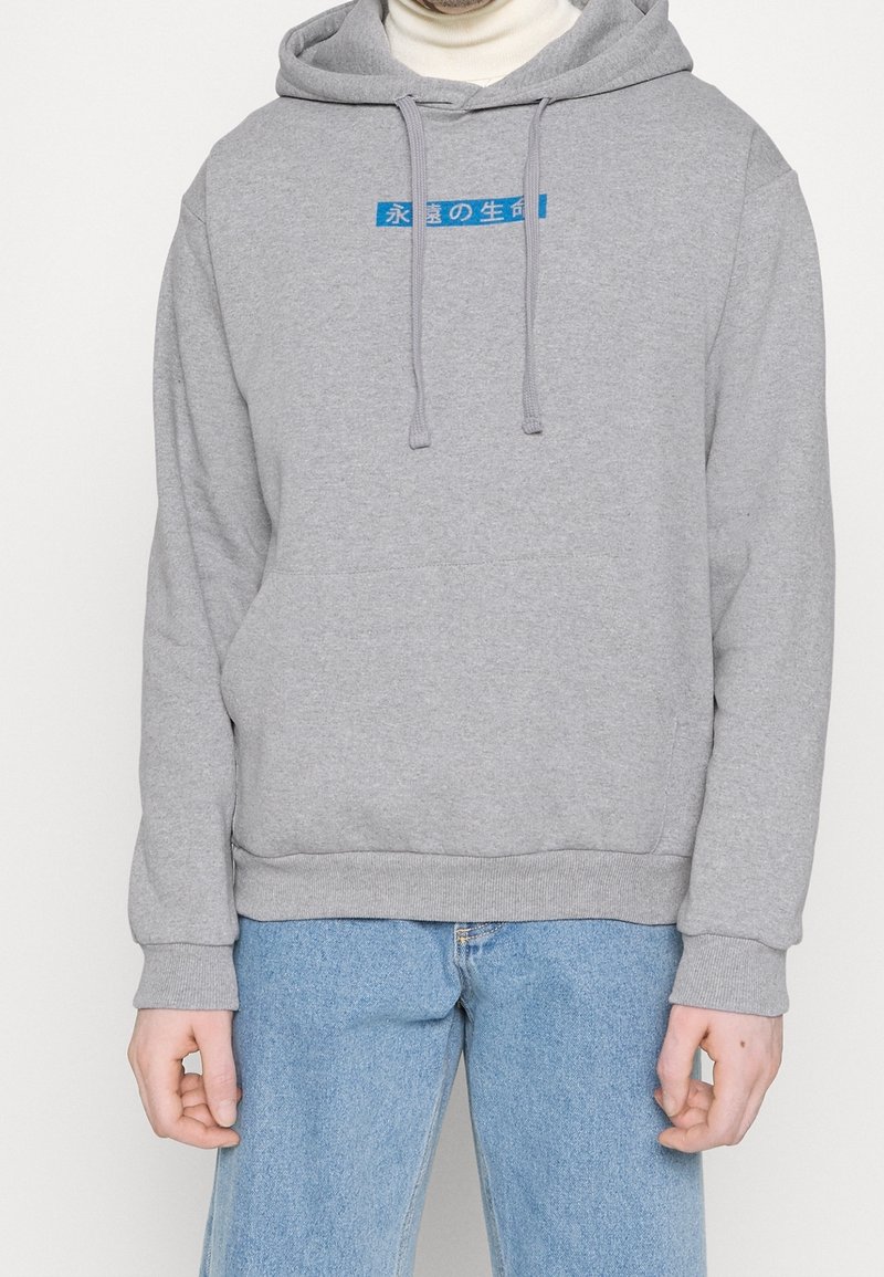 Sweat à capuche gris en tissu doux, avec une poche kangourou à l'avant, des cordons de serrage et un texte bleu sur la poitrine.