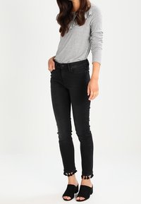 Top gris de manga larga con canalé, vaqueros negros ajustados con dobladillo rizado y mules negros destalonados con tacón de bloque.