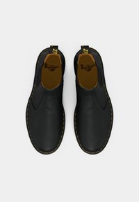 Chaussures à enfiler en cuir noir avec finition texturée, couture jaune autour de la semelle et languette de traction jaune contrastante au talon.