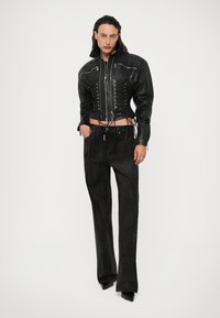 Jachetă scurtă din piele neagră cu detalii lace-up în față, asociată cu pantaloni din suede negri cu un model texturat.
