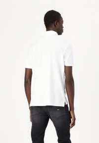 Hvid polo t-shirt med korte ærmer og krave, parret med mørke jeans. T-shirten har en lige pasform og har sideskår.