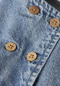 Džinsa audums gaiši zilā tonī ar teksturētu virsmu. Aprīkots ar četriem apaļiem koka pogām ar caurumu rakstu.