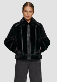 Schwarze Kunstpelzjacke mit einem breiten Kragen, vorderem Reißverschluss und Lederelementen. Hat eine kastige Passform und eine weiche Textur.