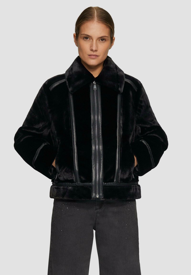 Schwarze Kunstpelzjacke mit einem breiten Kragen, vorderem Reißverschluss und Lederelementen. Hat eine kastige Passform und eine weiche Textur.