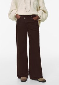 Pantaloni a gamba larga in corduroy marrone con vita alta, caratterizzati da un design a cinque tasche e bottoni metallici a contrasto, abbinati a un maglione in maglia a trecce.