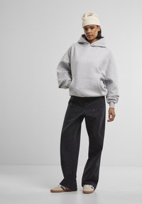 Grau Hoodie mit Kängurutasche und gerippten Bündchen, kombiniert mit dunklen, weiten Hosen und beigen Sneakern. Eine hellfarbige Strickmütze rundet den Look ab.