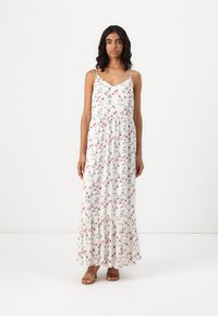 Blommig maxiklänning i vit tyg, med rosa och gröna blommor, spagettiaxlar, en åtsittande bodice och volangkant i flera lager.