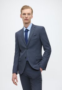 Fato azul-marinho com acabamento texturizado, casaco de botão único, lapelas de corte reto e calças correspondentes. Camisa de tom azul claro e gravata escura incluídas.