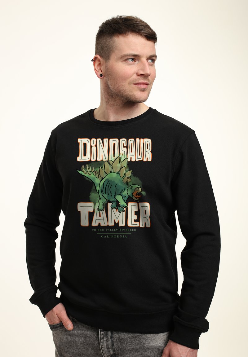Felpa nera con una grafica che presenta un dinosauro verde e la scritta "Domatore di Dinosauri". Polsini e orlo a coste, texture morbida.
