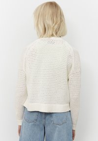 Maglione a maglia leggero di colore crema con un design a trama aperta e testurizzata, maniche raglan e orlo a coste. Abbinato a pantaloni corti in denim blu a vita alta.