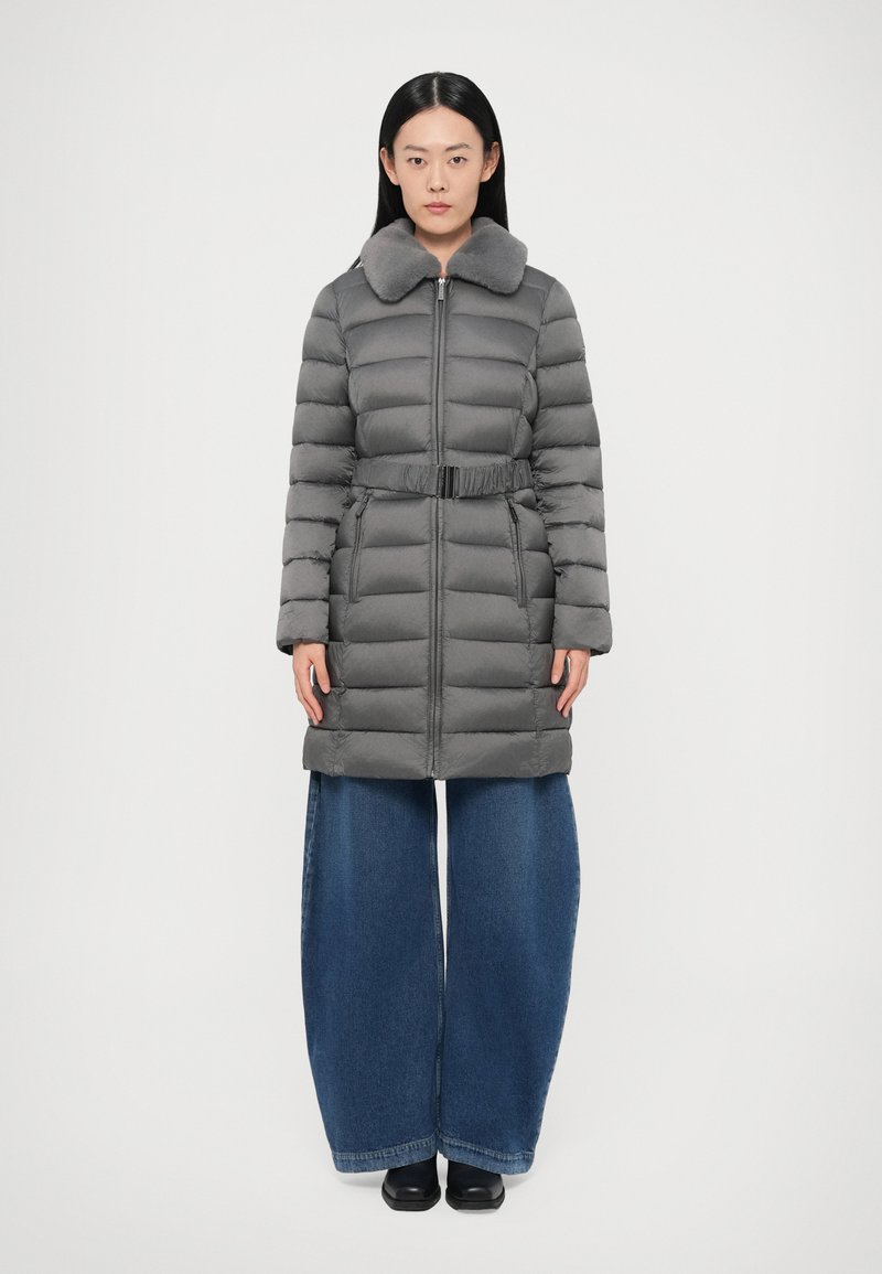 Γκρι μπουφάν τύπου puffer με γουνάτο για�κά, κλείσιμο με φερμουάρ, ρυθμιζόμενη ζώνη και καπιτονέ σχέδιο, φορεμένο πάνω από μπλε τζιν παντελόνια με φαρδύ πόδι και μαύρα παπούτσια.