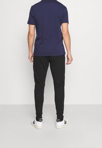 Marineblaues Baumwoll-T-Shirt, schwarze Slim-Fit-Hosen und weiße Sneaker mit schwarzen Akzenten. Einfaches Design, minimale Details, keine sichtbaren Muster.
