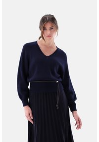 Marineblauer Strickpullover mit V-Ausschnitt und Ballonärmeln, kombiniert mit einem plissierten schwarzen Rock. Verfügt über einen Bund mit Kordelzug.