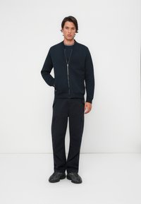Veste zippée bleu marine avec des poignets côtelés, assortie à un pantalon cargo. Le tissu semble doux ; le pantalon comporte des poches latérales et a une coupe décontractée.