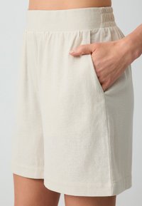 Beige linnen shorts met een elastische taille, zijzakken en een relaxte pasvorm. De stof heeft een subtiele textuur en een gladde afwerking.