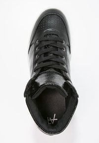 Svart högsko med en texturerad, glänsande ovandel som har perforeringar, platta skosnören och en vadderad insida. Genomskinlig yttersula.