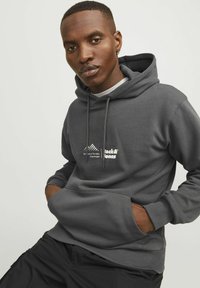 Szara bluza z kapturem z przednią kieszenią typu kangur. Posiada logo w białym i żółtym kolorze na klatce piersiowej oraz sznurki na kapturze.